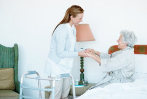 A female caregiver practices safe strategies for lifting and transferring seniors while helping an elderly female client out of bed.