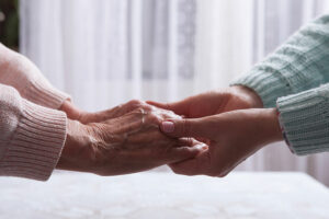 A woman and her aging mother, who is experiencing mental health concerns, hold hands.