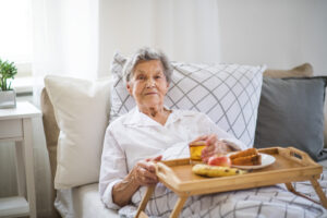  An older woman sits in bed with a tray of food on her lap as she struggles with decreased appetite, one of several common end-of-life changes people may face.