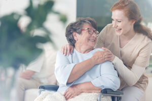 An older woman in a wheelchair smiles at her in-home caregiver who is trained in empowering senior independence.