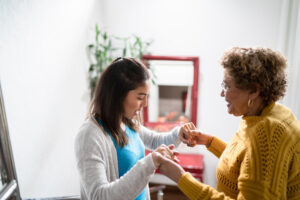 An older woman living with multiple sclerosis holds the hands of her caregiver.